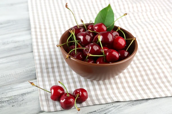 Fresh cherries in bowl with napkin on wooden table, closeup — Stock Photo, Image