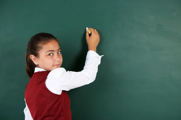 Schönes kleines Mädchen schreibt auf Tafel im Klassenzimmer — Stockfoto