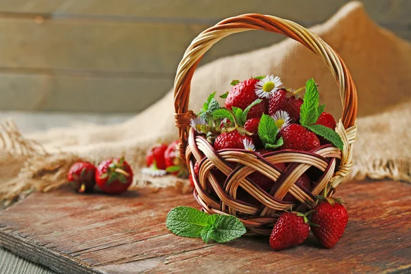 Fraises mûres rouges dans un panier en osier, sur fond de bois — Photo