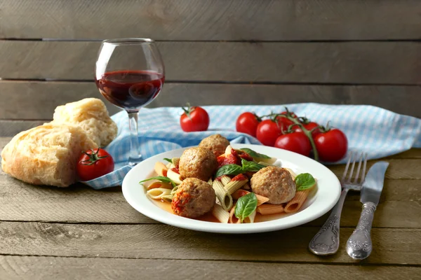 Паста с фрикадельками на тарелке, бокал красного вина на фоне деревянного стола — стоковое фото