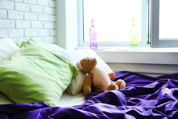 Удобная кровать с подушками и плюшевым мишкой в спальне — стоковое фото