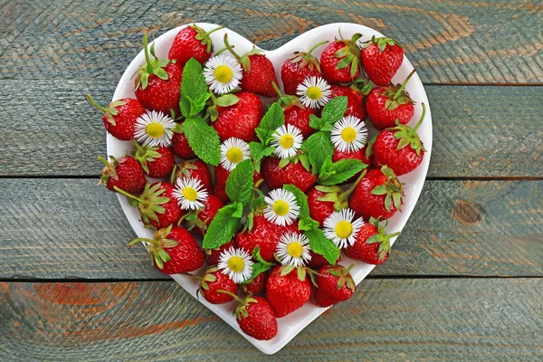Rote reife Erdbeeren auf herzförmigem Teller, auf farbigem Holzhintergrund — Stockfoto