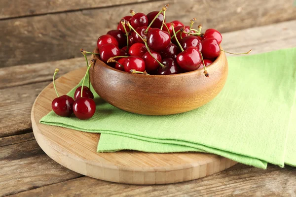 Fresh cherries in bowl with napkin on cutting board on wooden background — Stock Photo, Image