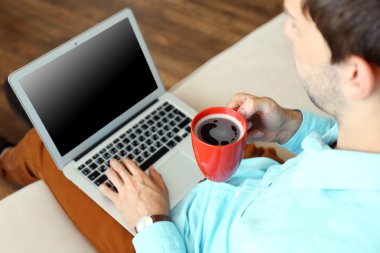 Odasında kanepede dizüstü bilgisayar ile çalışan adam