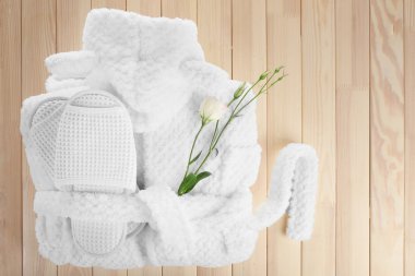 Bathrobe, towel and slippers on wooden table, top view clipart