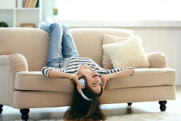 Mulher ouvindo música em fones de ouvido enquanto deitada no sofá no quarto — Fotografia de Stock
