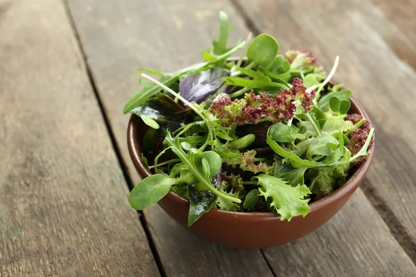 Fresh mixed green salad in bowl on wooden table close up — Stock Photo, Image