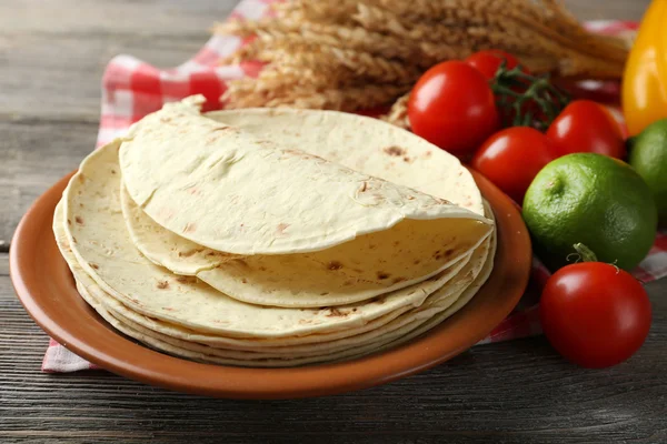 Stack of homemade whole wheat flour tortilla and vegetables on plate, on wooden table background — Stock Photo, Image