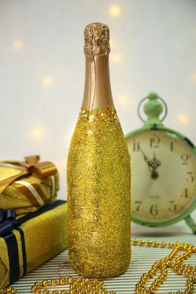 Ozdobne butelki szampana z obecnych skrzynek, koraliki i zegar na jasnym tle — Zdjęcie stockowe