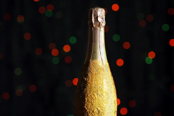 Декоративная бутылка шампанского на темном цветном фоне с пятнами — стоковое фото