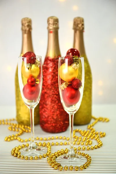 Dekorativa champagne flaskor med pärlor och julgranskulor på ljus bakgrund — Stockfoto