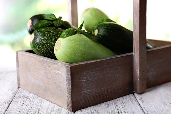 Courgettes fraîches avec courge et basilic dans une boîte en bois sur fond lumineux — Photo