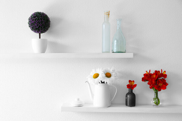 Decorative vases with flowers on wooden shelf