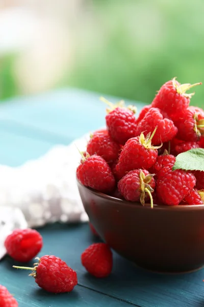 Fresh raspberries in bowl on wooden table on blurred nature background — Stock Photo, Image