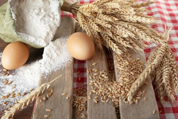 Whole flour with wheat and eggs on wooden table, closeup — Stock Photo, Image