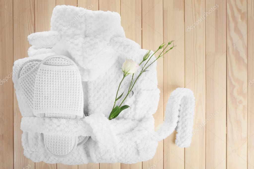 Bathrobe, towel and slippers on wooden table, top view