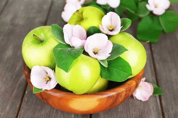 Manzanas frescas con flor de manzana en tazón, sobre mesa de madera —  Fotos de Stock