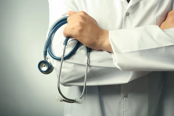 Médico masculino segurando estetoscópio em fundo cinza — Fotografia de Stock