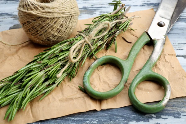 Rosemary sprigs with rope and scissors on parchment on wooden table, closeup — Stock Photo, Image