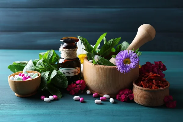 Hierbas, bayas, flores y píldoras sobre fondo de mesa de madera de color — Foto de Stock