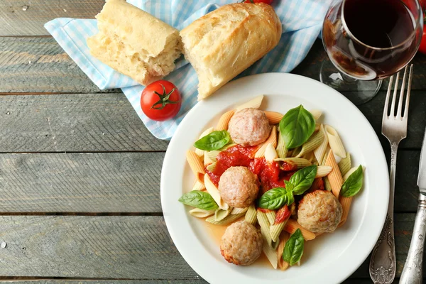 Pasta con albóndigas en plato, copa de vino tinto sobre fondo de mesa de madera — Foto de Stock