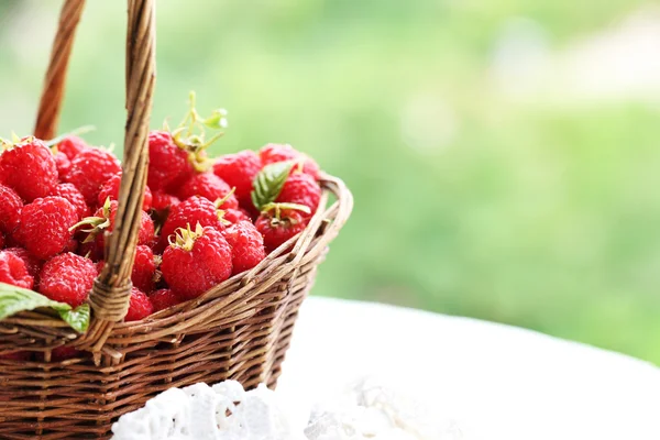 在木制的桌子上模糊的自然背景上的柳条篮子里的新鲜树莓 — 图库照片