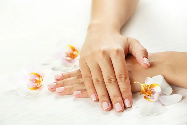 Mãos da mulher com manicure francês e flores do orchid na tabela de madeira close-up — Fotografia de Stock
