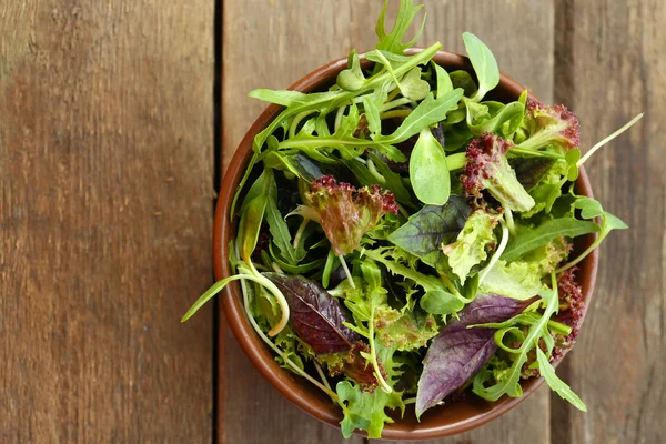 Färsk blandad grönsallad i skål på träbord nära håll — Stockfoto