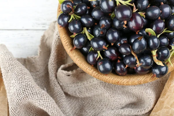 Mogna svarta vinbär i trä skål på säckväv, närbild — Stockfoto