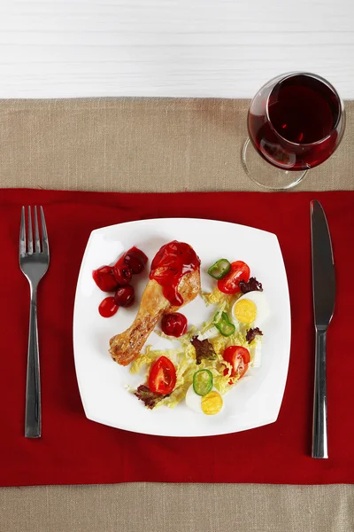 Dish of baked chicken leg and vegetable salad in white plate with glass of wine on table with napkin, top view — Stock Photo, Image