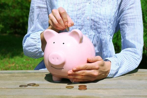Hand putting coin into pink piggy bank — Stock Photo, Image