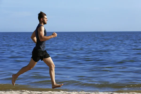 Ung man joggar på stranden — Stockfoto