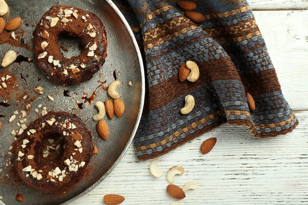 Deliciosos donuts com cobertura de chocolate e nozes na mesa de perto — Fotografia de Stock