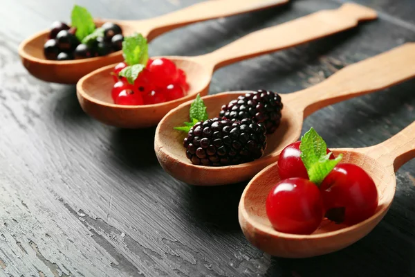 Forest berries in wooden spoons on color background — Stock Photo, Image