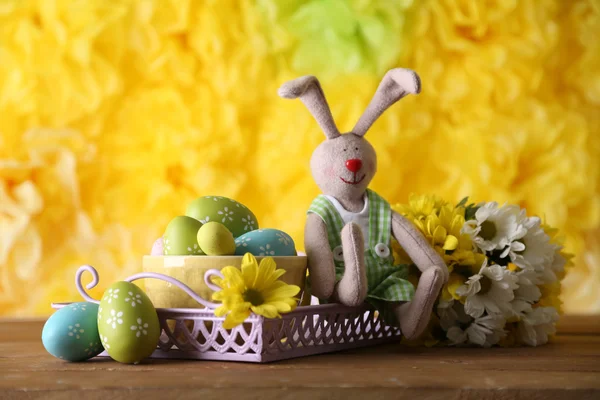 Påskharen med målade påskägg med blommor på träbord på gul bakgrund — Stockfoto