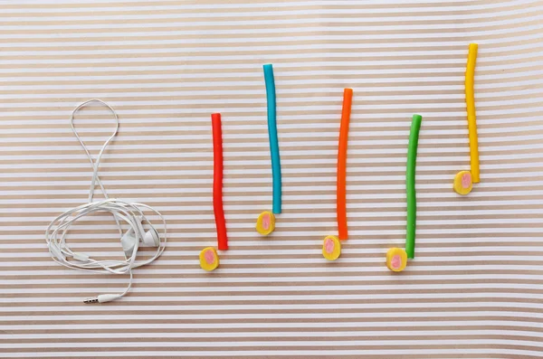 Treble clef with musical notes of candies and headphones on striped background — Stock Photo, Image