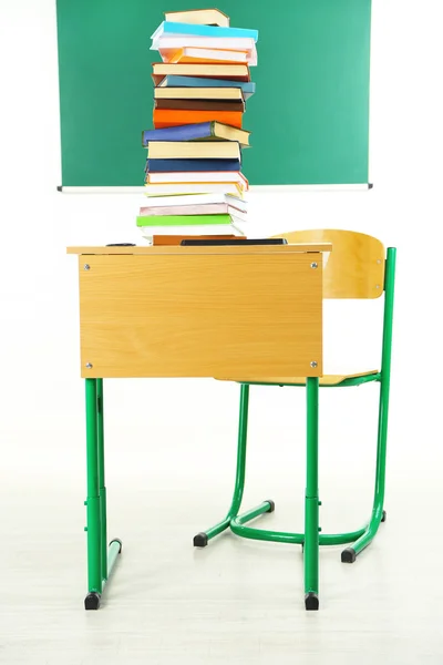 Wooden desk with books and chair in class on blackboard background — Stock Photo, Image