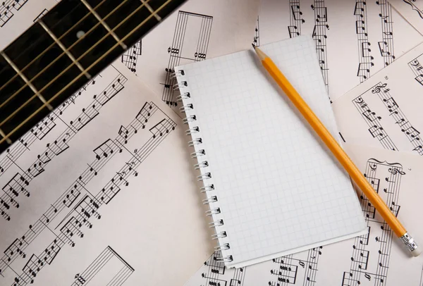 Scena di registrazione musicale con chitarra e blocco note su sottofondo di fogli musicali — Foto Stock