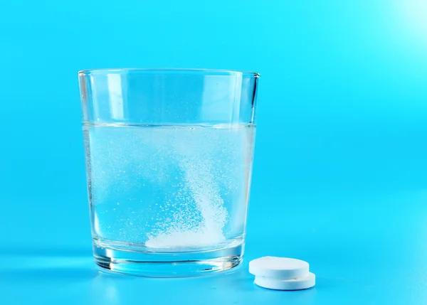 Verre d'eau et pilules sur fond bleu — Photo