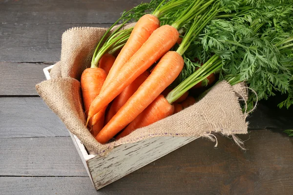 Fresh organic carrots in box with sackcloth on wooden background — Stock Photo, Image