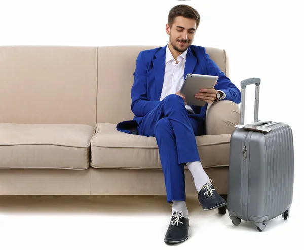 Homme d'affaires avec valise et tablette assis sur canapé isolé sur blanc — Photo