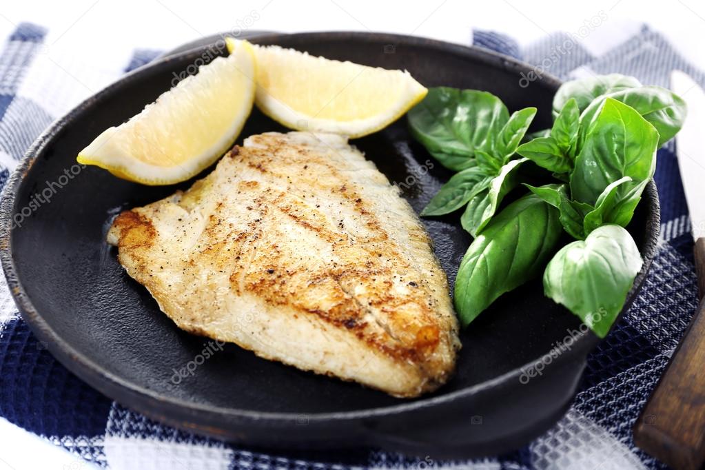 Dish of fish fillet with basil and lemon on table close up