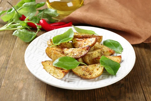 Patate al forno con foglie di basilico in piatto bianco sul tavolo di legno, primo piano — Foto Stock