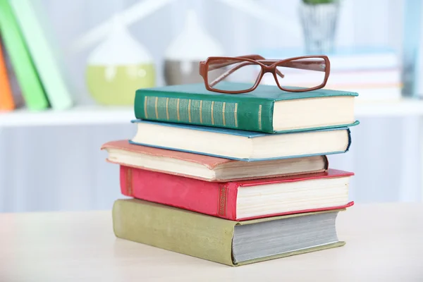 Stoh knih s brýlemi na dřevěný stůl v pokoji — Stock fotografie