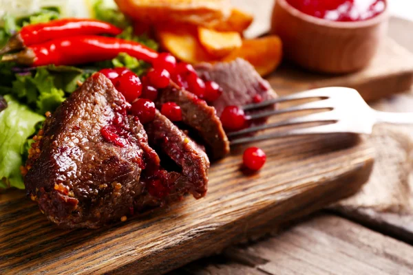 Carne com molho de cranberry, fatias de batata assadas na tábua de corte, no fundo de madeira — Fotografia de Stock