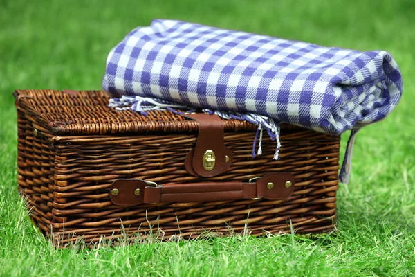 Rieten picknickmand en plaid op groen gras, buitenshuis — Stockfoto