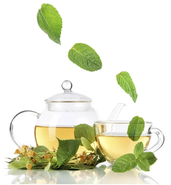 Bouilloire et tasse de thé avec tilleul et feuilles de menthe tombantes isolées sur blanc — Photo