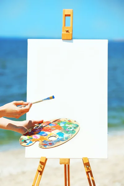 Hand holding palette with paints and easel — Stock Photo, Image