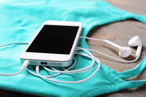 Teléfono móvil y auriculares con camiseta en mesa de madera, primer plano —  Fotos de Stock