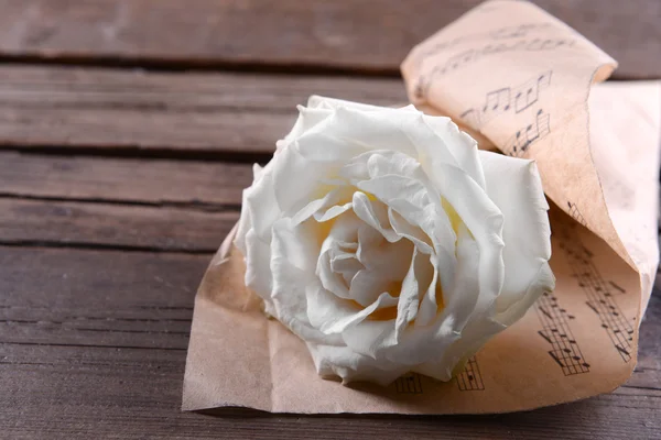 Hermosa rosa envuelta en hoja de música sobre fondo de madera —  Fotos de Stock